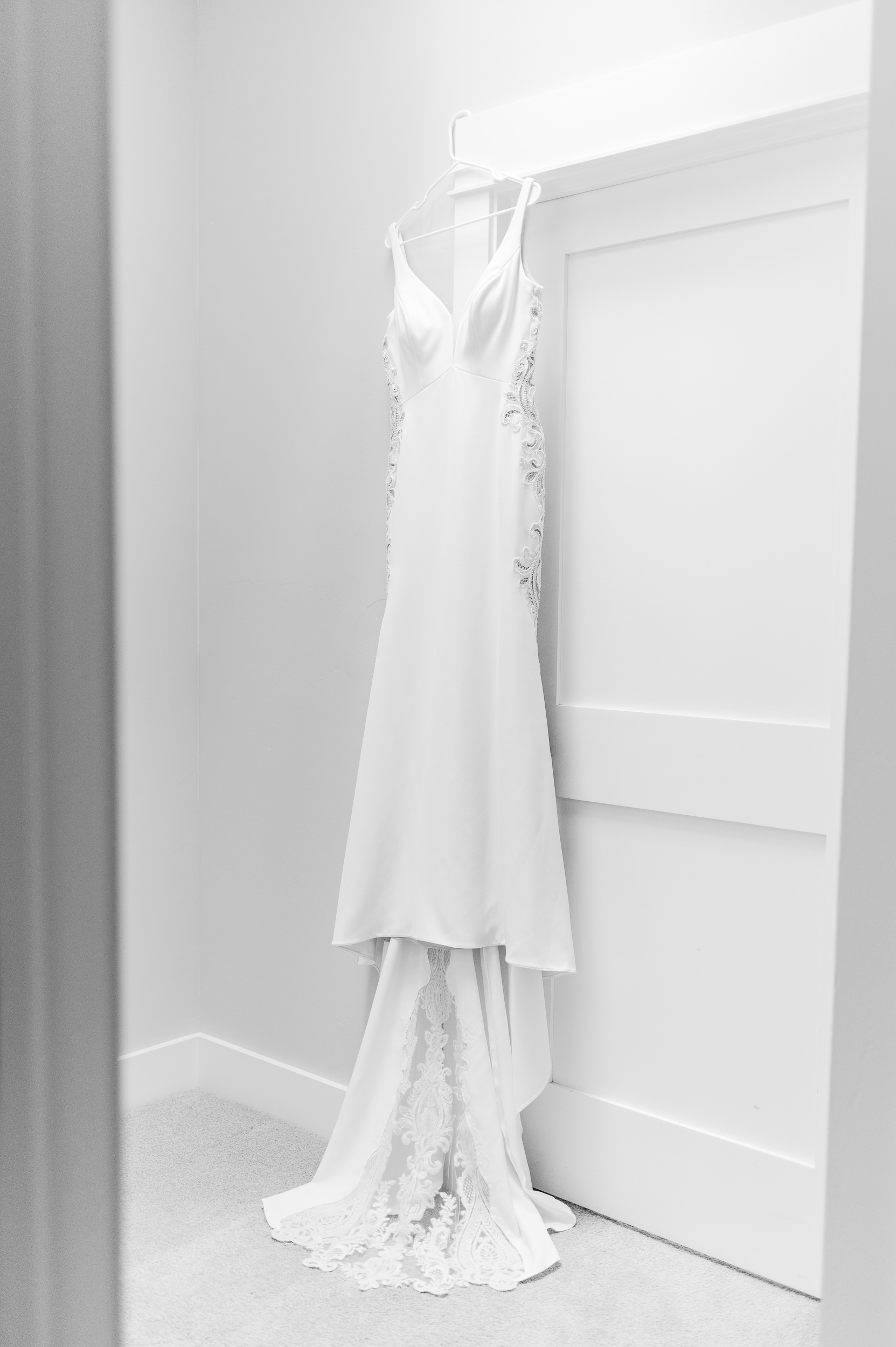 A white wedding dress hanging on a door frame in a hallway.