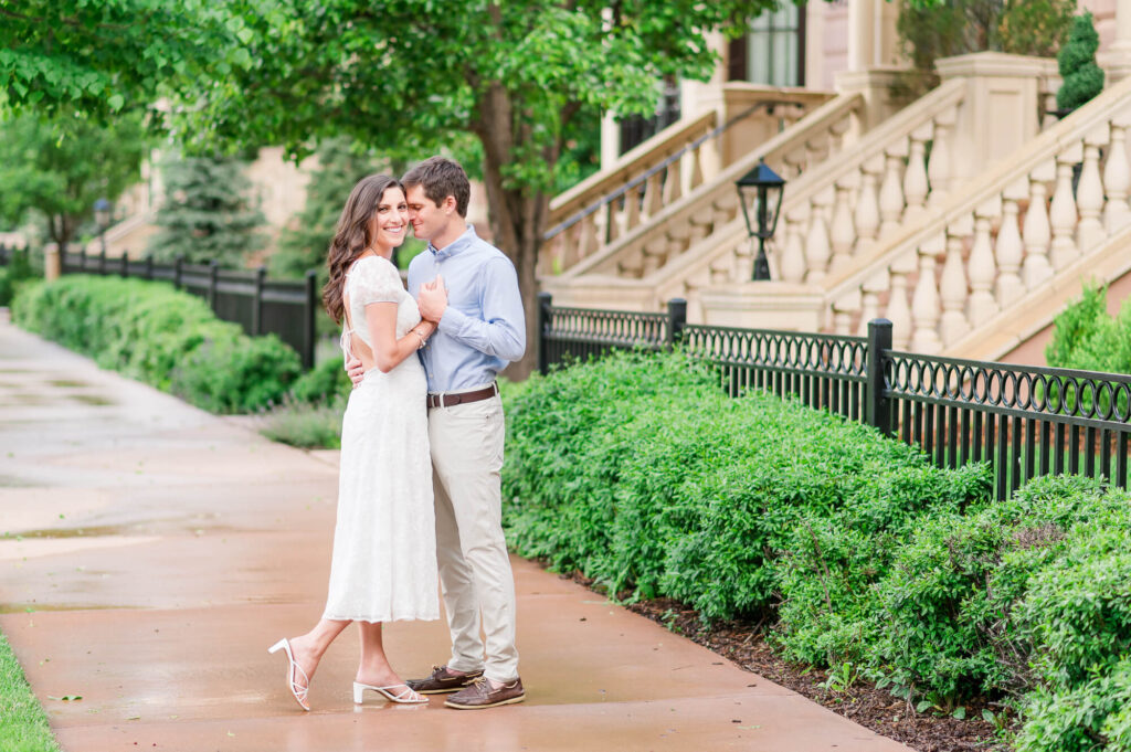 A couple poses on a sidewalk next to the Broadmoor Hotel in Colorado Springs on a cloudy day during their engagement photos.