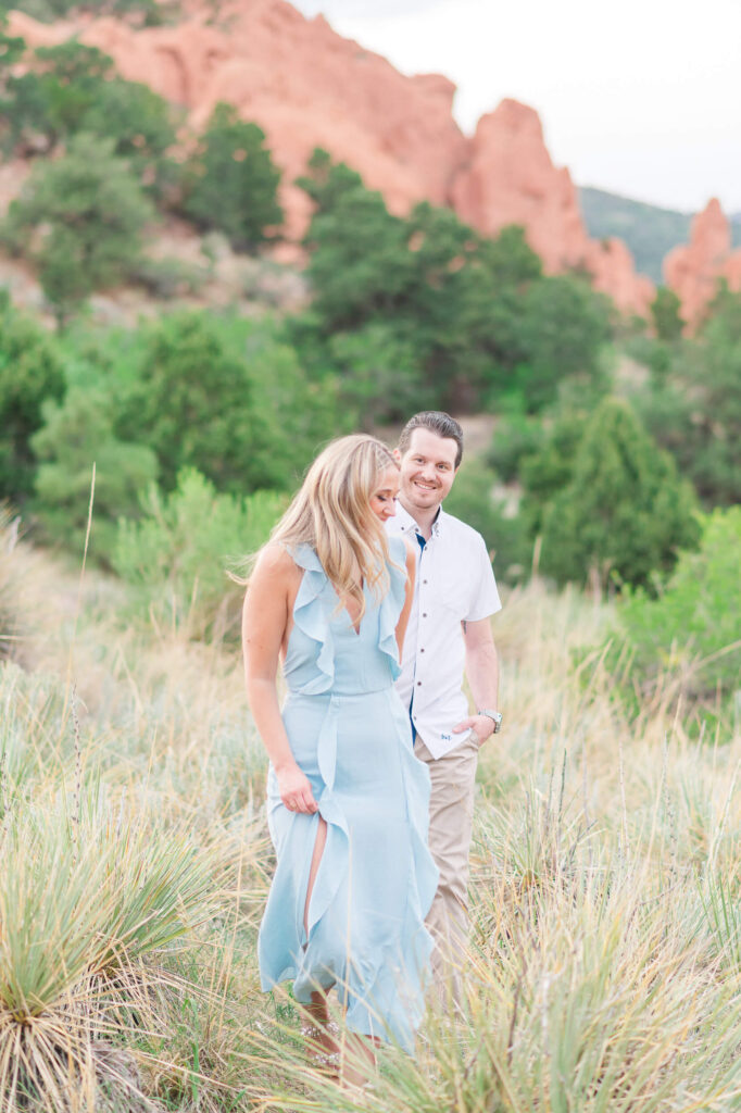 A man and woman walk through a field at Garden of the Gods during their engagement photos in Colorado Springs.