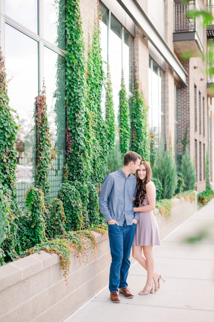 A couple poses in downtown Colorado Springs next to a building covered with ivy.