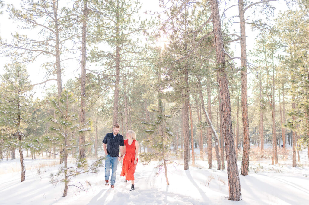A couple walks through a snowy forrest during their engagement photos at Fox Run Park in Colorado Springs.