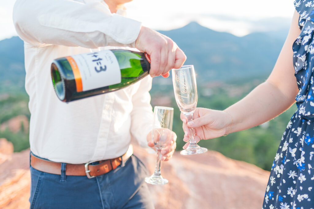 A man pours champagne into a glass held by his fiance during their engagement session at Garden of the Gods.