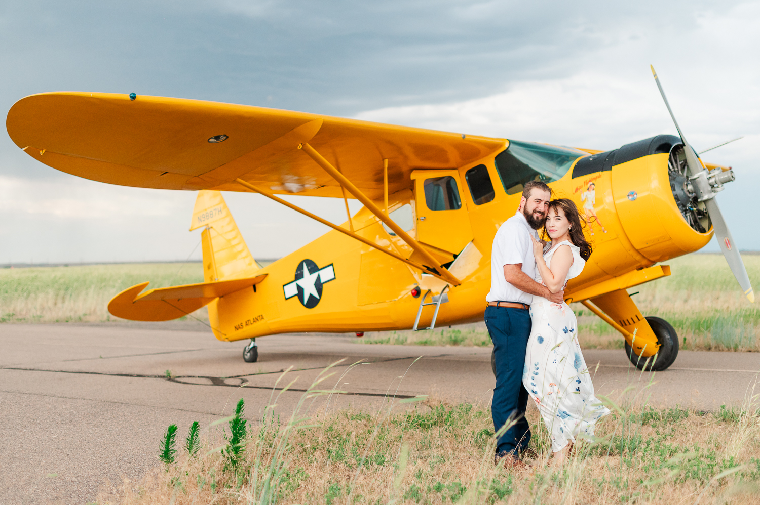 Couple stands in front of a yellow airplane on the runway during their engagement session.