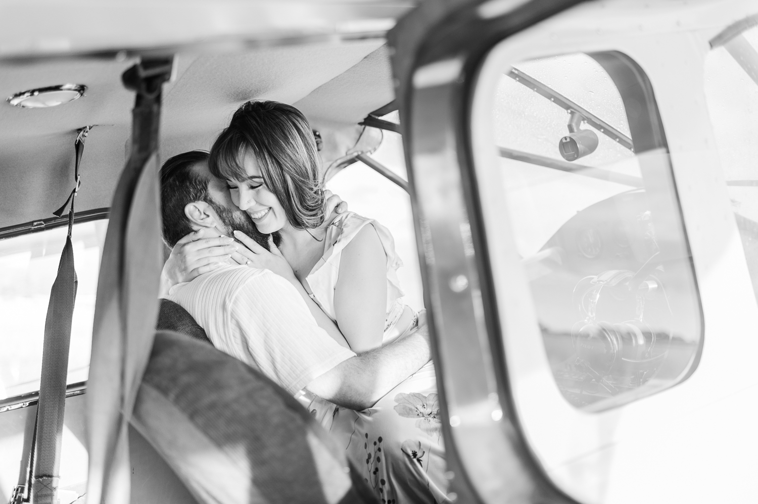 A woman smiles while sitting on her fiance's lap inside a private airplane during their engagement photos.