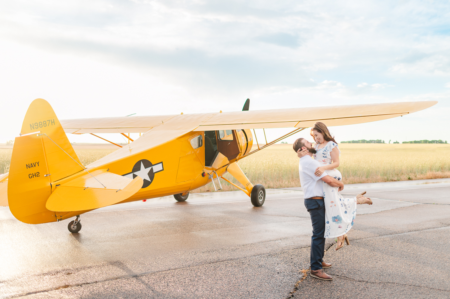 A man picks up a woman in front of a yellow airplane on a runway north of Denver.