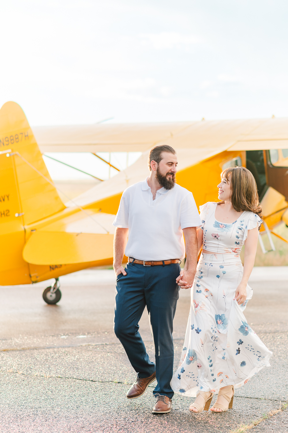 Couple walks next to a yellow vintage airplane.