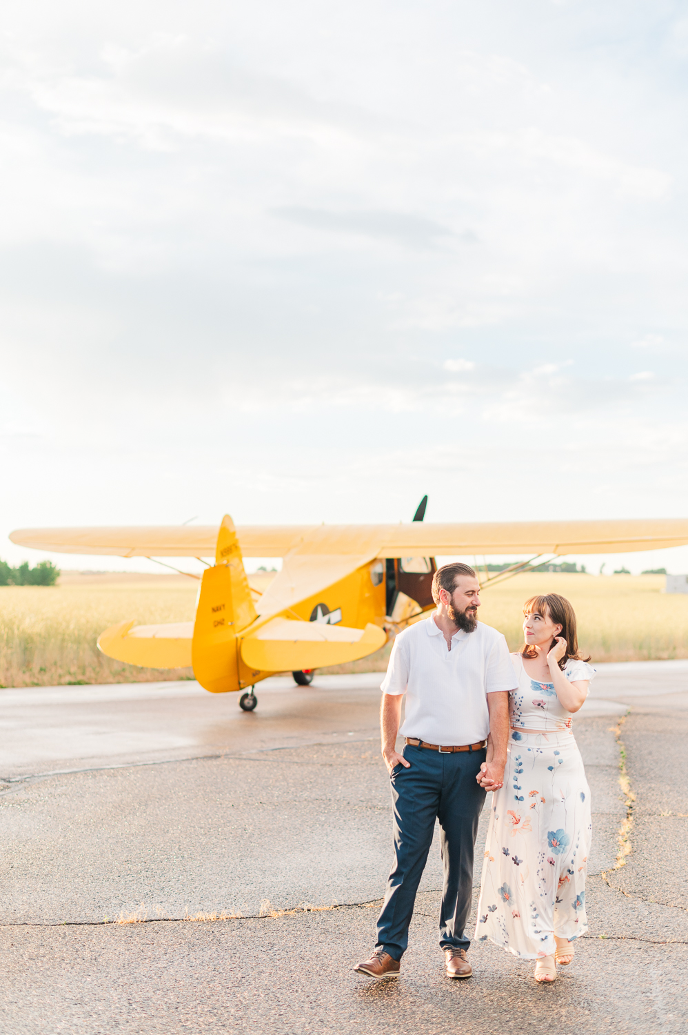 Man and woman walk hand in hand away from the yellow airplane in the background.