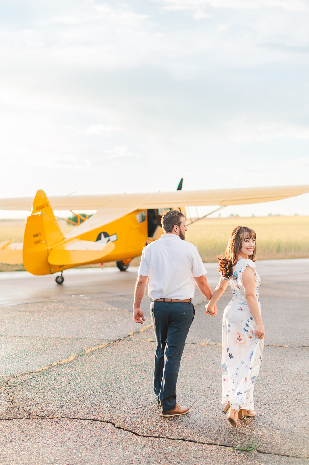 A couple walks down a paved road towards a yellow airplane.