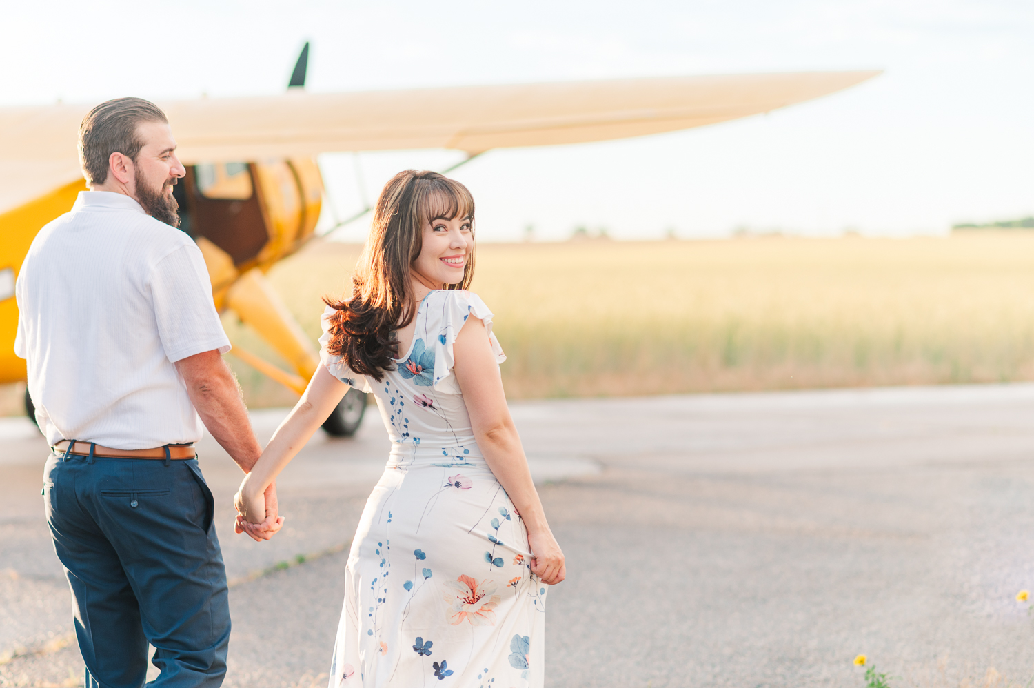 Couple walks toward a yellow airplane on a runway.