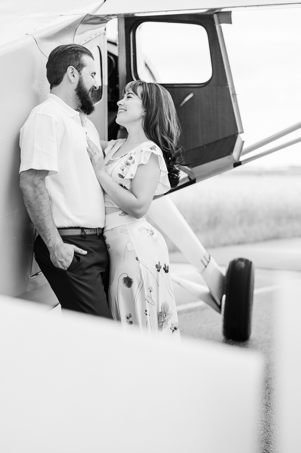 Couple smiles at each other while leaning against a vintage airplane.